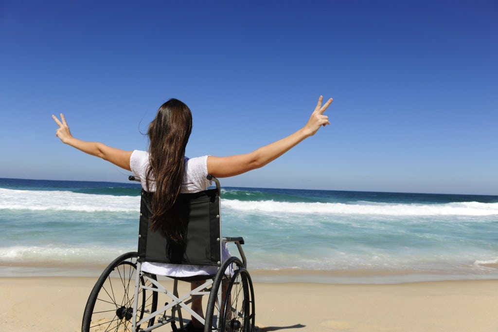 happy woman in wheelchair outdoors beach showing victory sign