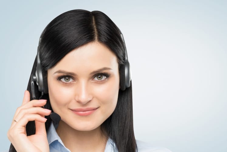 Front view of the smiling brunette support phone operator with headset. Light blue background.